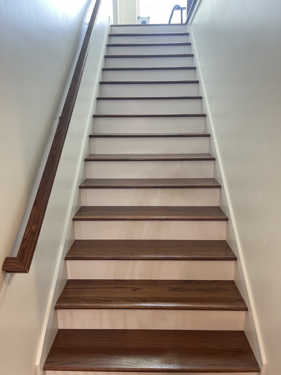 Finished staircase with stained treads and handrail, crisp white risers, and painted walls